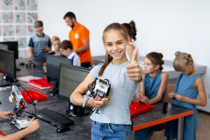 Portrait of a happy schoolgirl girl in a robotics class, she holds a robot assembled from plastic parts programmed on a computer